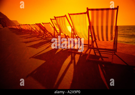 Vereinigtes Königreich. England. Reihe von Liegestühlen direkt an Strandpromenade beleuchtet wieder bei Sonnenuntergang. Stockfoto