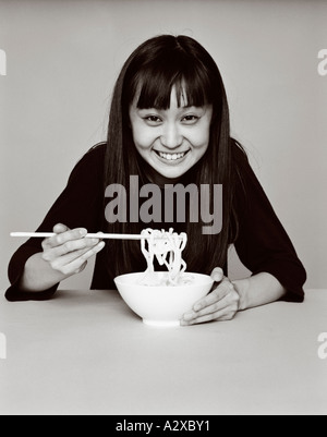 Junge Frau sitzt drinnen essen von Schüssel Nudeln. Stockfoto
