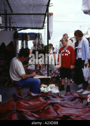 dh Handwerk Marktstand TEGUISE LANZAROTE Sonntag Markt Stall Straßenverkäufer Leder Sitze junge Käufer beobachten Stockfoto