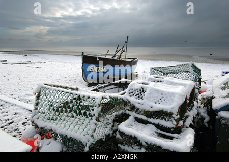 Schnee auf ein einsames Fischerboot und ein Haufen von Hummer Töpfen auf Worthing Strand nach Winterstürme in Sussex und Kent Stockfoto