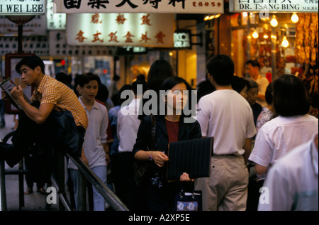 MANN SITZT HUPEN IM GESCHÄFTIGEN STRAßENSZENE MIT BLICK AUF JUNGE GESCHÄFTSFRAU, LESEN KONG 1996 Stockfoto
