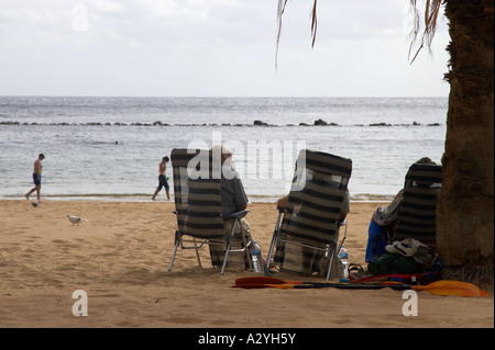 ältere Menschen sitzen in Liege-Stühle bergende unter Palmen am Strand Stockfoto