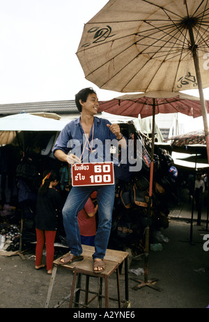 Mann auf einem Hocker mit Preis Schild um den Hals Werbung Schnäppchen in den Chatuchak Weekend Market in Bangkok Stockfoto