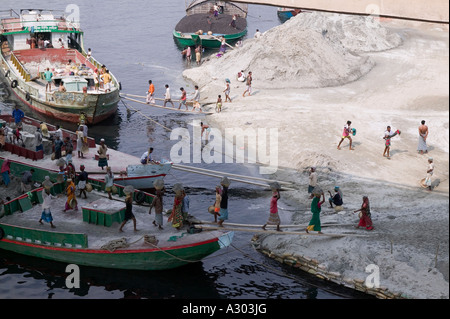 Arbeiter tragen schwere Körbe Sand auf ihre Köpfe aus dem Boot an den Strand entlang der Straße zum Savar in Bangladesch Stockfoto