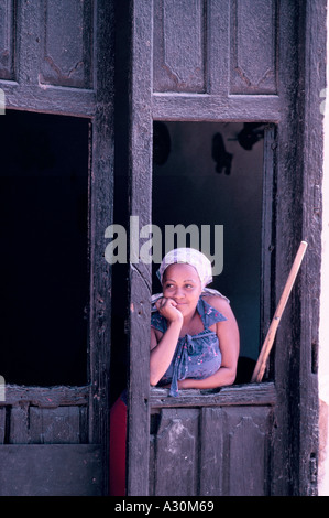 Junge kubanische Frau mit Kopftuch, Blick aus einem hölzernen Fensterrahmen in einer Tür in Trinidad, Kuba Stockfoto