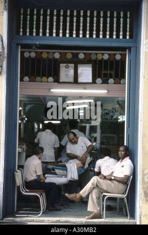 Friseure in Santiago, Kuba am Werk. Männer sitzen auf Stühlen am Eingang warten ihrerseits Stockfoto