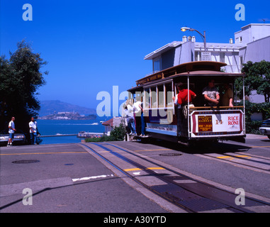 Ein San Francisco Tram Car klettert einen steilen Hügel mit Blick auf Alcatraz Gefängnis Insel in der Ferne Stockfoto