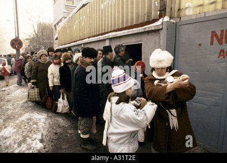 Rumänien nach der Revolution Mädchen Mutter mit Armen voller Dosen, hilft wie andere Menschen stehen Schlange stehen für Essen auf der Straße vor Geschäft Gebäude Bukarest 1990 Stockfoto