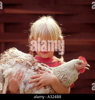 Kleine blonde Mädchen mit zwei Zöpfen eine Henne in ihren Armen halten Stockfoto