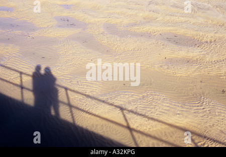 Schatten der beiden Figuren und Promenade oder Pier Geländer auf nassen wellige hellen Sand Mondlandschaft ähnelt Stockfoto