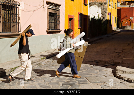 Mexiko San Miguel de Allende Mann und Frau Fuß über die Straße tragen Kartons und Papierrollen für die Verpackung Stockfoto