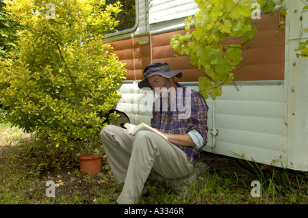 Herr Mann sitzt vor einem alten Wohnwagen, ein Buch zu lesen Stockfoto