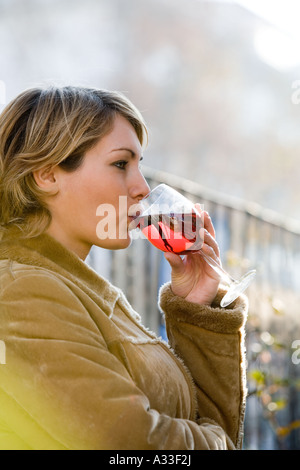 Eine junge kaukasischen blonde Frau trinken Rotwein, leichten braunen Mantel. Frau im Fokus Stockfoto