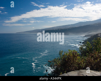 Morgennebel gegen dunkle Klippen mit intensiv blauen Meer und Himmel und hellen weißen Wolken und Surf, Puerto De La Cruz, Teneriffa Stockfoto