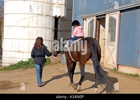 Drei Jahre altes Mädchen reiten eine Pferd Mutter führt Stanhope Ställe Huntington NY Stockfoto