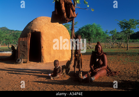 Frau des Stammes Himb oder Ovahimba sitzen vor ihrer Hütte mit ihren Kindern im Inneren Kraal Kaokoveld Namibia Afrika Stockfoto