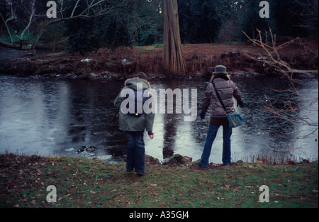 Besucher, die Steinwürfe auf einem zugefrorenen See in Kew Gardens, Surrey, UK Stockfoto