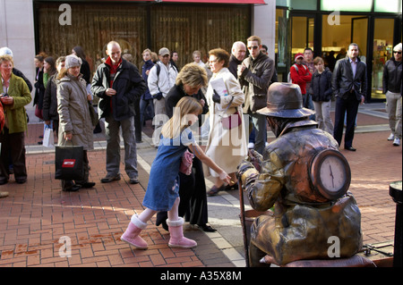 Touristen stehen herum, wie Frau und junges Mädchen Straßenkünstler gekleidet wie eine Metall-Statue Spenden Stockfoto