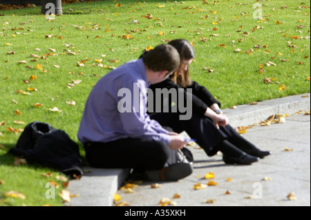 männliche und weibliche Freunde in Tiefe Diskussion sitzen auf den Bordstein in der Nähe von grünen Rasen und Laub im Herbst Stockfoto