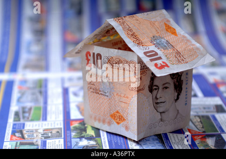 Ein Haus aus zehn Pfund-Noten sitting on Top of Eigenschaft anzeigen in einer Zeitung, die Immobilienpreise und Hypotheken Stockfoto