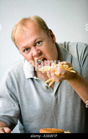 Mann schaut in die Kamera, als er eine Handvoll Pommes frites gierig in den Mund stopft Stockfoto