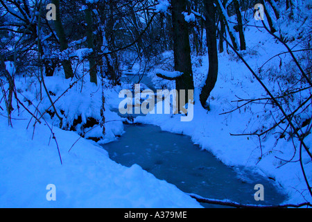 Gefrorener Bach schlängelt sich durch einen verschneiten Wald in Tschechien. Stockfoto