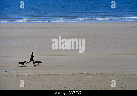 Mann läuft am Strand mit zwei Hunden Rest Bay Porthcawl Wales UK Stockfoto