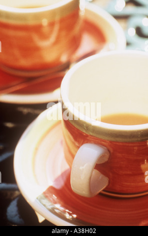 Nahaufnahme von zwei orange Tassen mit Untertassen mit Tee oder Kaffee Bodensatz auf einem dunklen Grün Schmiedeeisen Tisch Stockfoto