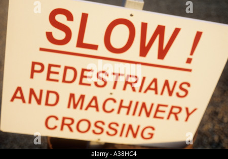 Streut gemalten weißen Schild mit roten Großbuchstaben Warnung Fahrer langsam Fußgänger und Maschinen Kreuzung Stockfoto