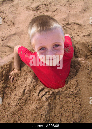 Ein vier Jahre alter Junge mit Beinen im Sand vergraben Stockfoto