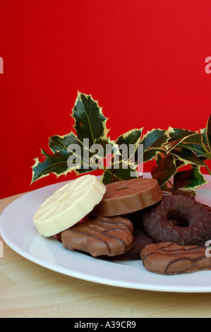 Schokoladenkekse auf einem weißen Teller mit einem roten Hintergrund mit holly Stockfoto