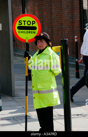 Einer britischen Lollipop Kreuzung Gardistin Kinderhilfe überqueren eine viel befahrenen Straße in London UK Stockfoto