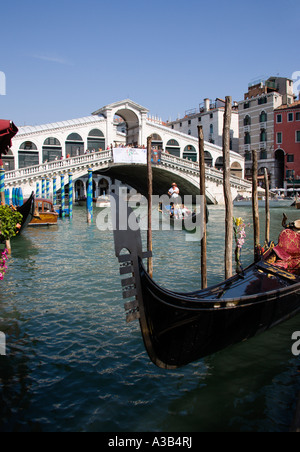 Italien Venetien Venedig Gondel vertäut am Canal Grande mit einem anderen tragenden Touristen Rialto-Brücke mit Menschen überfüllt Stockfoto