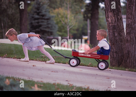 Schwester zieht ihr jüngeren Bruder, der in einem roten Wagen auf einem steilen Hügel sitzt Stockfoto