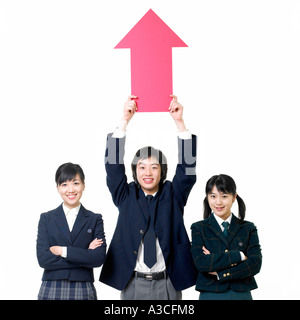 Ein männlicher Student hält einen roten Pfeil über dem Kopf und es gibt zwei Mädchen an seiner Seite Stockfoto