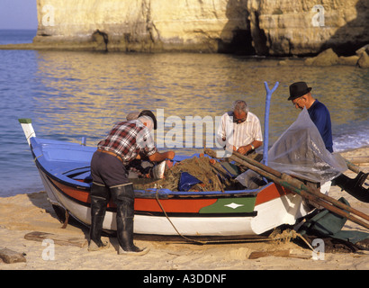 Carvoeiro Algarve Portugal Strand portugiesischen Fischer bei der Arbeit sprechen, auf bunten kleinen Fischerboot Prüfung Reparatur Fischernetze zusammenarbeiten Stockfoto