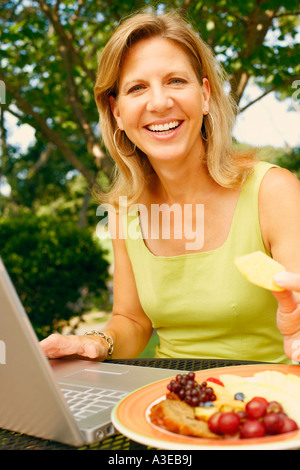 Porträt einer reifen Frau mit einem Laptop und Obstsalat zu essen Stockfoto