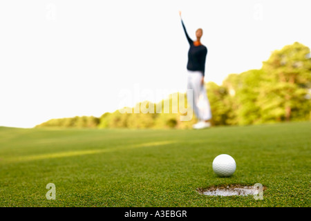 Nahaufnahme eines Golfballs am Rand eines Lochs mit einem Mann im Hintergrund Stockfoto