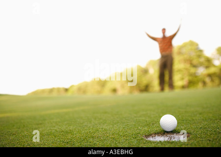 Nahaufnahme eines Golfballs am Rand eines Lochs mit einem Mann, der seine Arme im Hintergrund Stockfoto