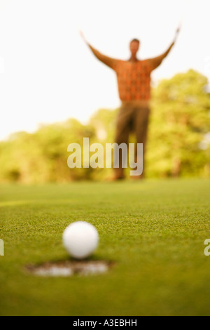 Nahaufnahme eines Golfballs am Rand eines Lochs mit einem Mann, der seine Arme im Hintergrund Stockfoto