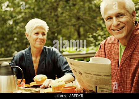 Porträt von einem reifen Mann lächelnd und halten eine Zeitung mit einer älteren Frau im Hintergrund Stockfoto