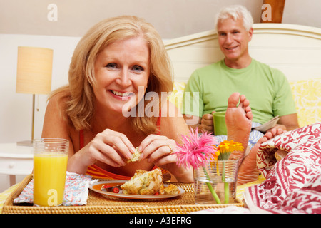 Porträt einer reifen Frau mit Frühstück im Bett mit einem reifen Mann, der hinter ihr sitzt Stockfoto