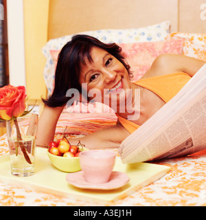 Porträt einer reifen Frau auf dem Bett liegend und halten eine Zeitung Stockfoto