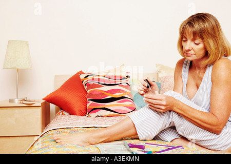 Reife Frau sitzt auf dem Bett Nagellack auftragen Stockfoto