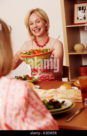 Reife Frau geben eine Schüssel mit Salat zu ihrer Freundin und lächelnd Stockfoto
