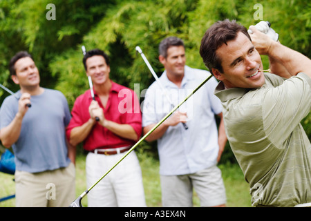Reifer Mann schwingt einen Golfclub mit seinen Freunden hinter ihm steht Stockfoto
