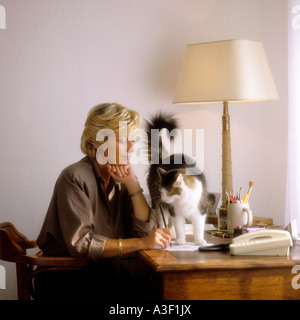 REIFE FRAU SCHREIBEN UND NEUGIERIGE KATZE ON DESK Stockfoto