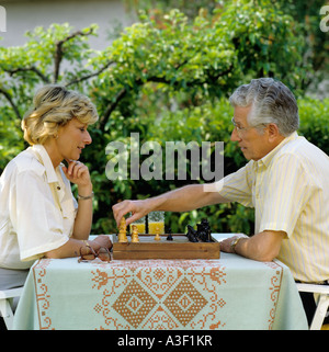 HERR ÄLTERES PAAR SPIELEN SCHACH IM GARTEN Stockfoto