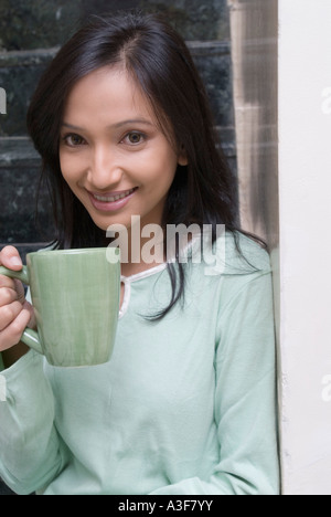 Porträt einer jungen Frau hält eine Tasse Kaffee und lächelt Stockfoto