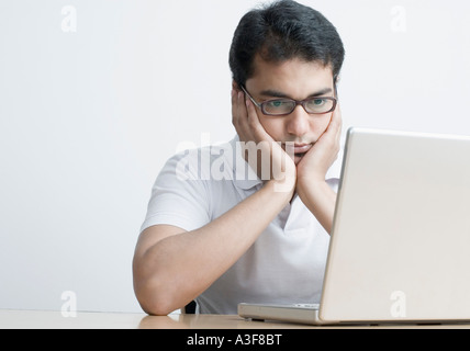 Ein junger Mann sitzt vor einem Laptop mit seinem Kopf in seine Hände in Nahaufnahme Stockfoto